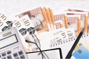 Ten pound notes with oficce items and a pair of reading glasses depict the concept of tax planning
